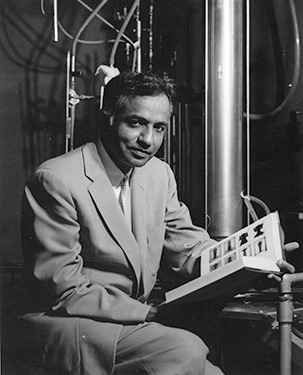 Subrahmanyan Chandrasekhar posing with open book. Equipment in the background is a Taylor-Couette apparatus built by Dave Fultz and Russ Donnelly at the University of Chicago.