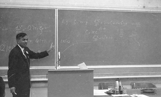 A black and white image of Subrahmanyan Chandrasekhar lecturing at a blackboard.