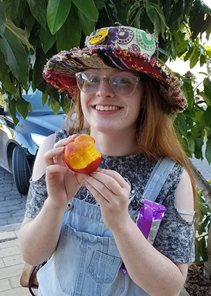 Rebecca Hughes wearing a sunhat and holding a piece of fruit