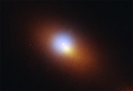 This is a composite image of the tidal disruption event AT2024tvd and the galaxy in which it is found.
The galaxy is somewhat elliptical in shape and larger from side to side than from top to bottom, as though it has been slightly squished. The galaxy presents itself as a hazy orange glow, observed in optical and ultraviolet light, surrounding a hazy, off-centered circle of blue-colored X-ray light.
Near the center of the blue circle of X-rays is a small, bright dot in ultraviolet light. This dot is AT2024tvd, the location where a black hole has torn apart a star roughly 2,600 light-years away from the center of the black hole's host galaxy. Most tidal disruptions have been detected at the centers of galaxies where supermassive black holes are usually found. The presence of a tidal disruption this far away from the center of the galaxy indicates the presence of a second large black hole in the region..